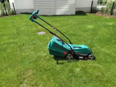 5 Best Lawn Mowers For Your Small Garden – Buying Guide : Bosch electric lawn mower in the middle of a grass lawn under the sun on a small garden